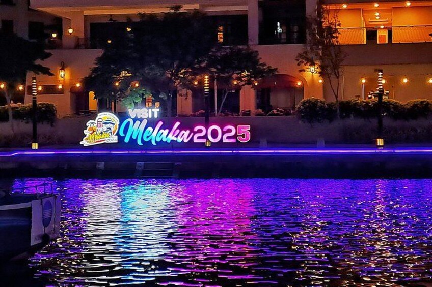 A neon sign with the text 'VISIT Melaka2025' and a reflection on water. 2