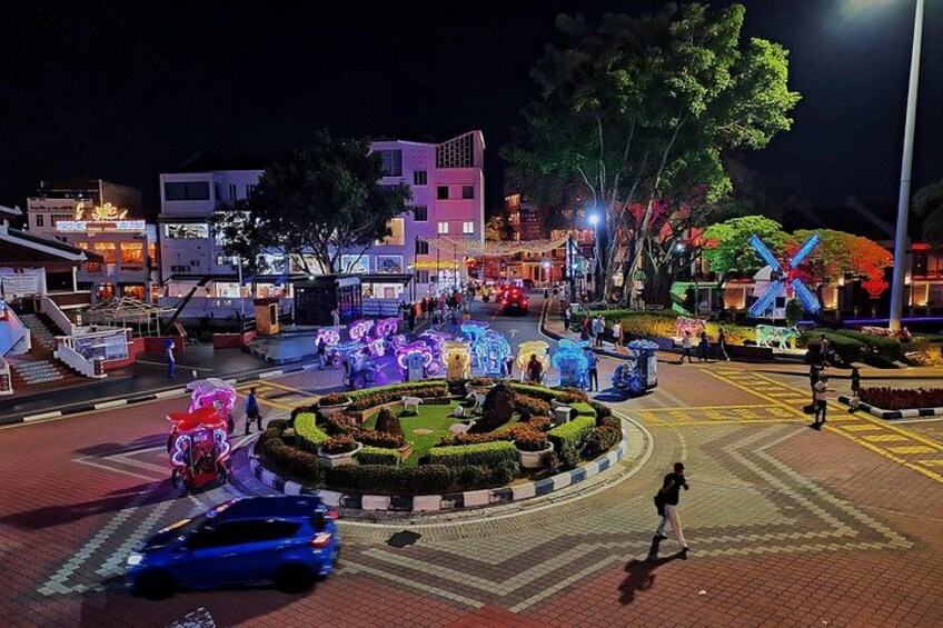 A well-lit urban square with decorative lights, a central garden, and surrounding buildings. 4
