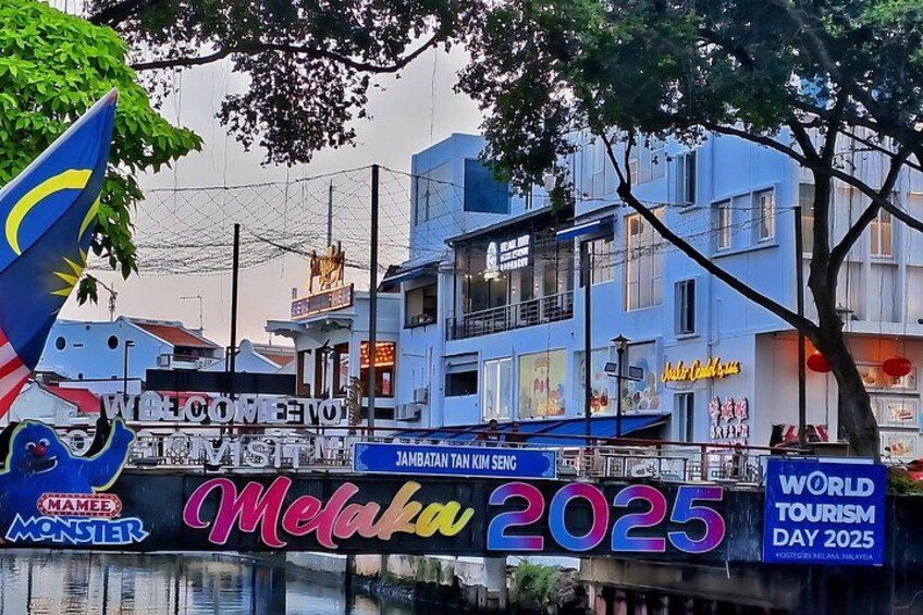 A waterfront with buildings, a sign for 'Melaka 2025,' and a Malaysian flag. 5
