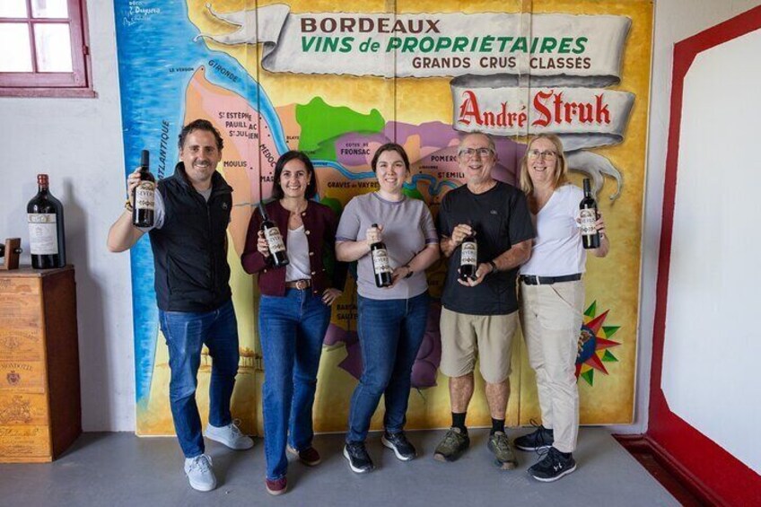 A group of people holding wine bottles in front of a backdrop with a map and text about Bordeaux wines. 1