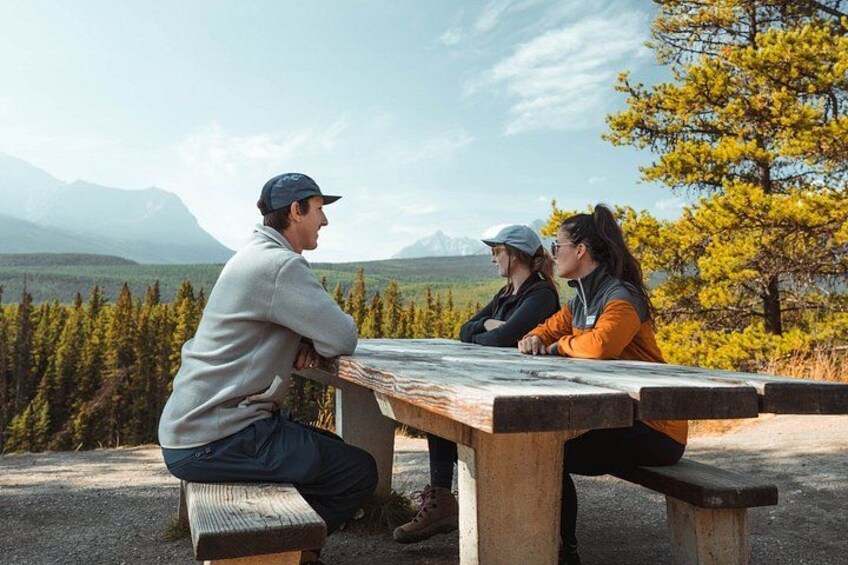 Three people sitting at a picnic table overlooking a mountainous landscape. 3