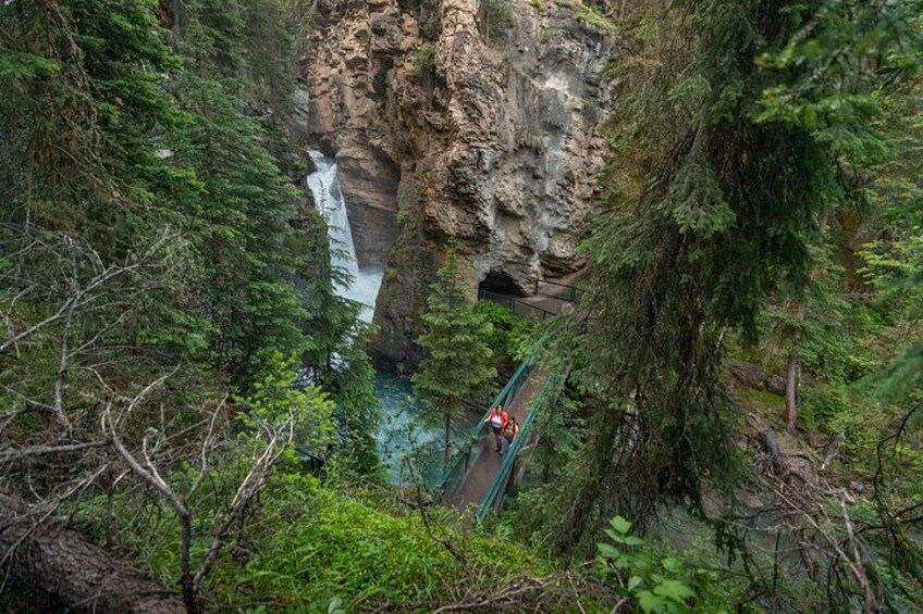 A person hiking on a bridge over a waterfall in a forested area. 5