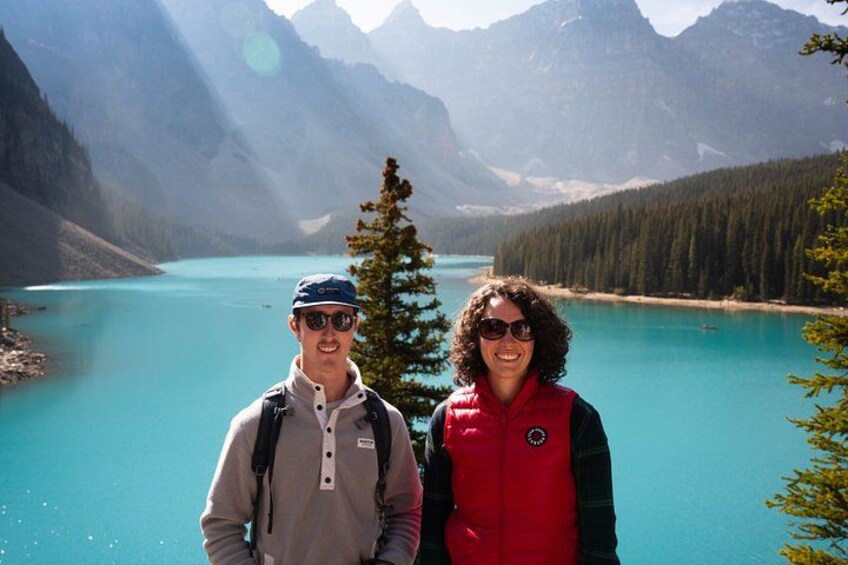 Two people standing in front of a turquoise lake surrounded by mountains. 2