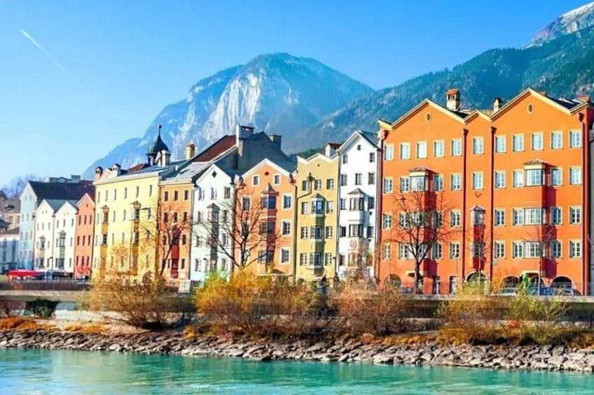 A row of colorful buildings by a river with mountains in the background. 2