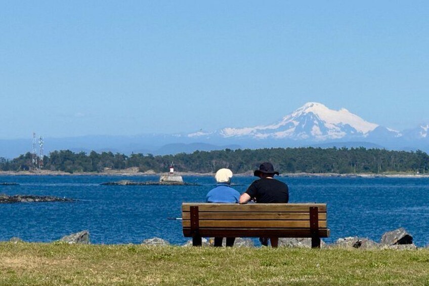 Zwei Personen sitzen auf einer Bank und blicken auf ein Gewässer mit einem Berg im Hintergrund. 3