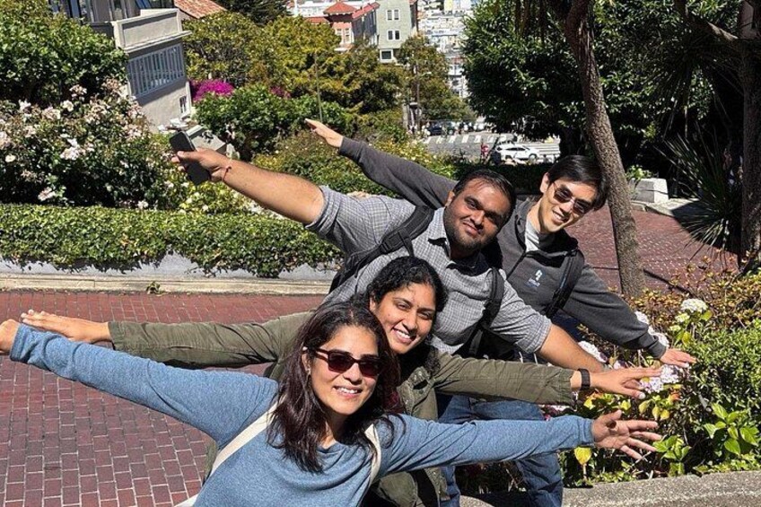 A group of people posing with outstretched arms in an urban park with brick pathways and greenery. 2