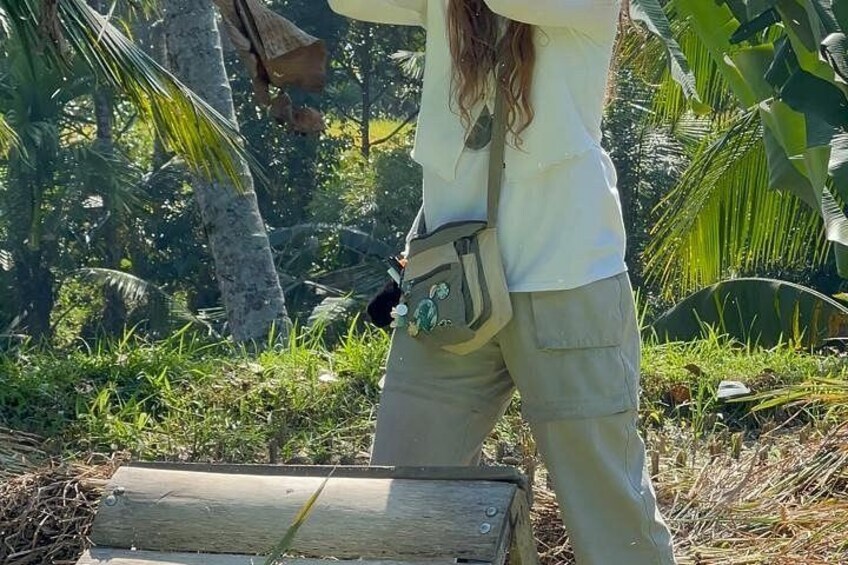 A person standing next to a wooden log in a tropical setting with palm trees and greenery. 3