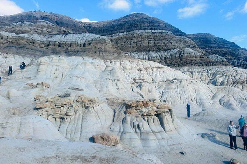 A rocky landscape with layered sedimentary formations and people exploring the terrain. 3