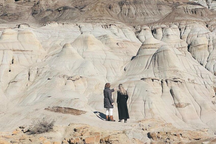 Two people standing on a rocky outcrop with layered sedimentary rock formations in the background. 4