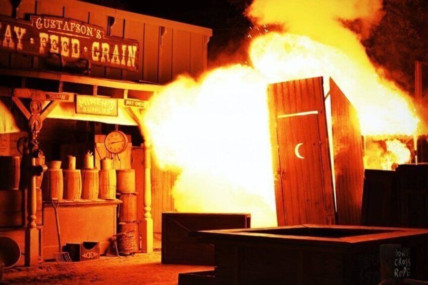A building with a sign that reads 'Gustafson's Hay Feed Grain' and a large fire burning in front of it. 3