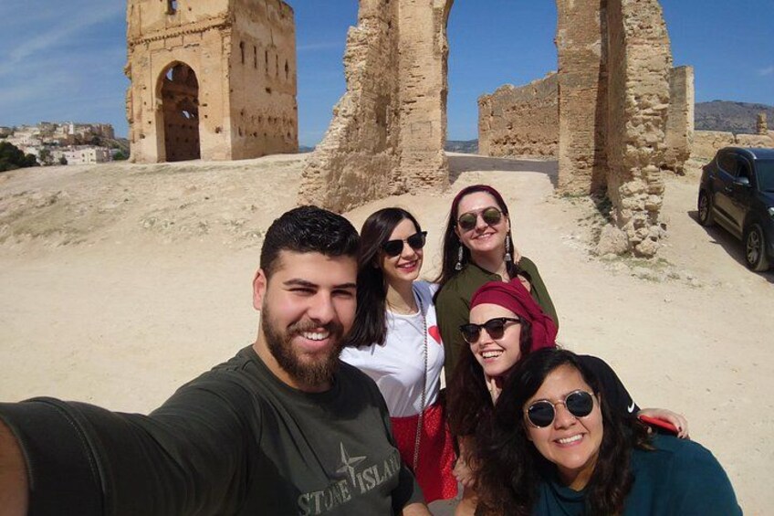 En grupp människor som tar en selfie framför antika ruiner, med ett torn och valv i bakgrunden. 3