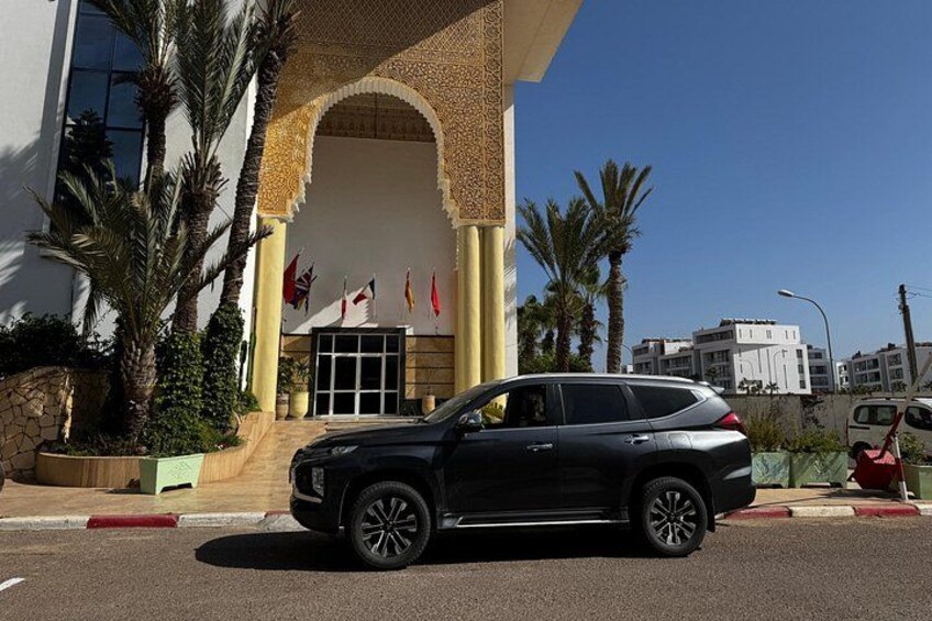 En svart SUV står parkerad framför en byggnad med en stor valvöppning och palmer. 1