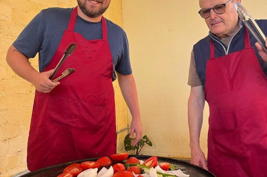 Twee mensen in schorten die kookgerei vasthouden, staan naast een barbecue met groenten. 3