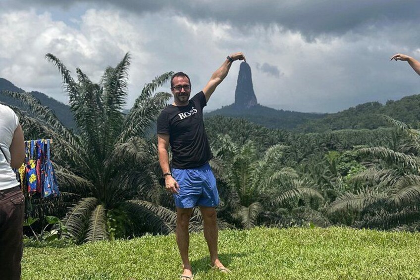 Eine Person steht in einer grünen Landschaft mit Palmen und einem Berg im Hintergrund. 5