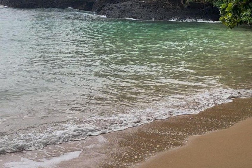 Ein Strand mit klarem Wasser, Wellen und einer felsigen Küstenlinie. 1