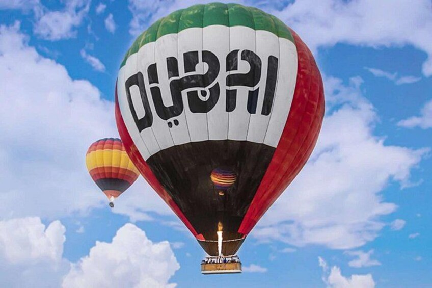 Two hot air balloons with Arabic text, one in the foreground and one in the background, against a blue sky with clouds. 3