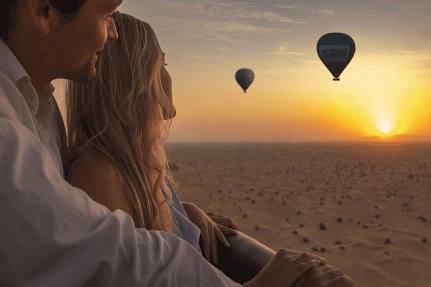 A couple sitting on a beach with hot air balloons in the background. 2
