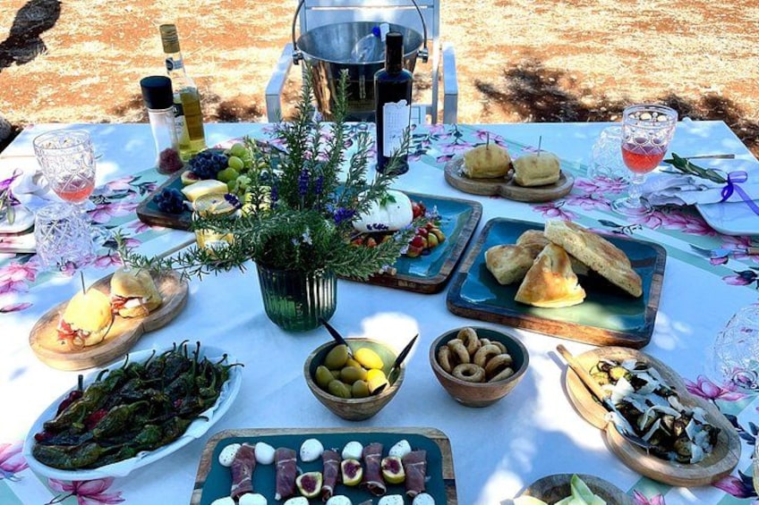 Mesa al aire libre con diversos alimentos, una botella de vino y una planta decorativa. 4