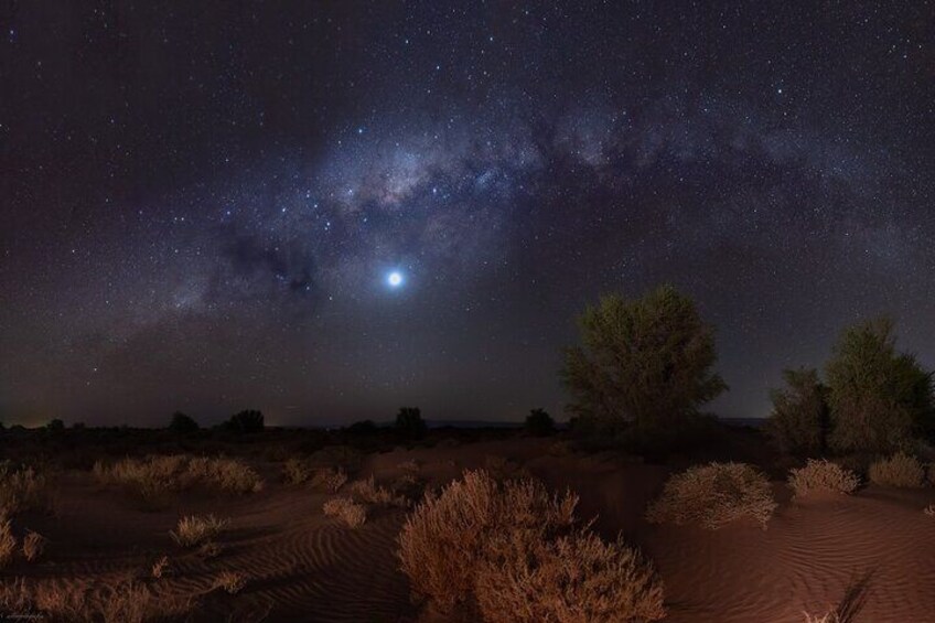 A desert landscape at night with a starry sky, including the Milky Way and a visible moon. 1