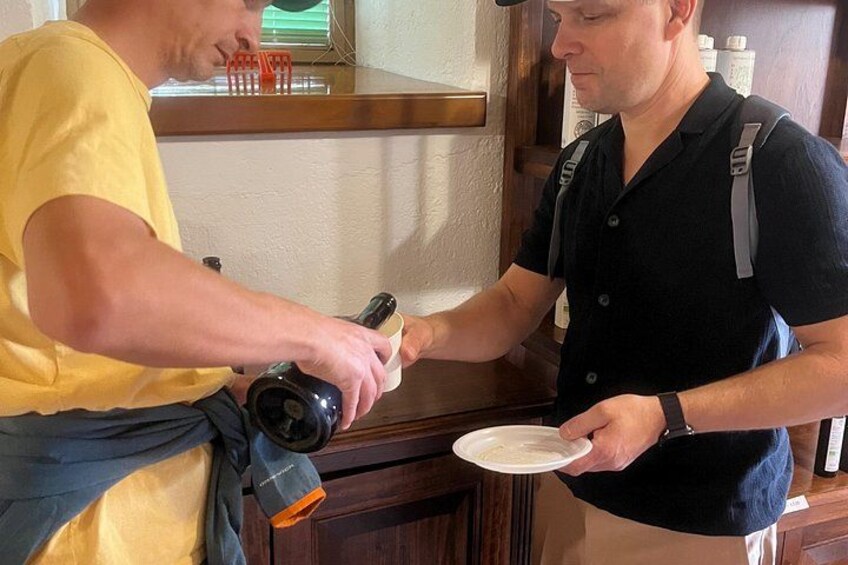 Two people in a kitchen, one handing a bottle to the other. 3