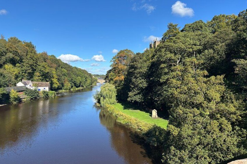 Un río con casas en la orilla izquierda, árboles densos en la derecha y un cielo azul despejado. 5