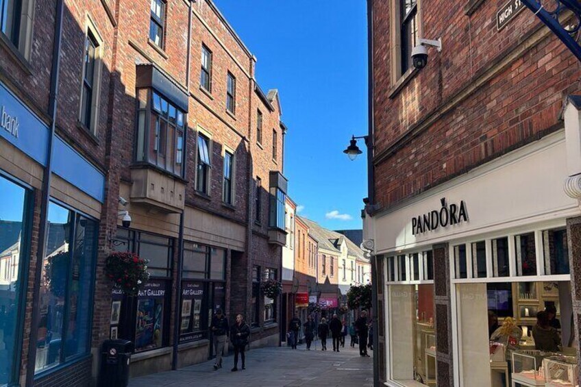 A street with shops, including a Pandora store, and pedestrians walking on the sidewalk. 5