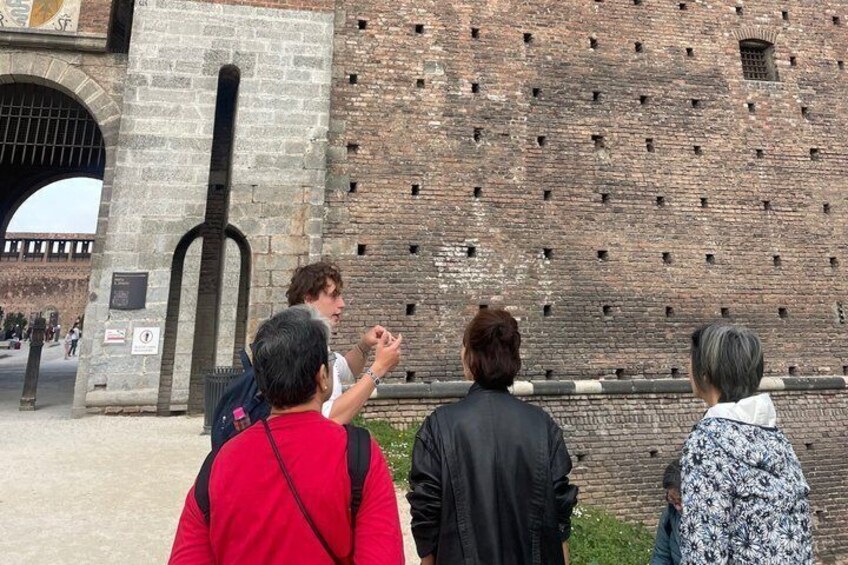 A group of people standing in front of a brick wall with a large arched entrance. 2