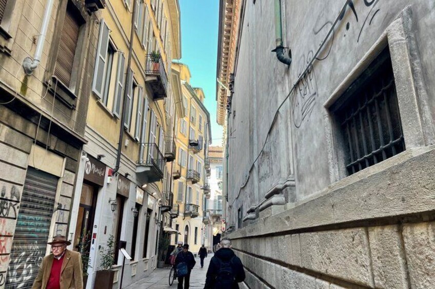 A narrow urban street with old buildings, a cyclist, and pedestrians. 4
