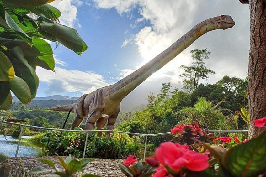 Eine lebensgroße Dinosaurierskulptur in einem üppigen Garten mit Teich und blühenden Pflanzen. 1