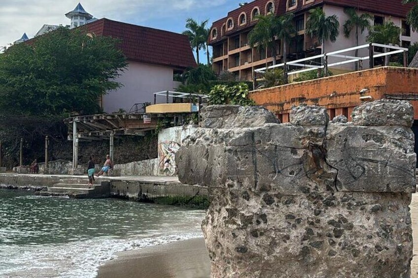 A stone wall by the water, a building with a red roof, and a person walking on a pier. 4