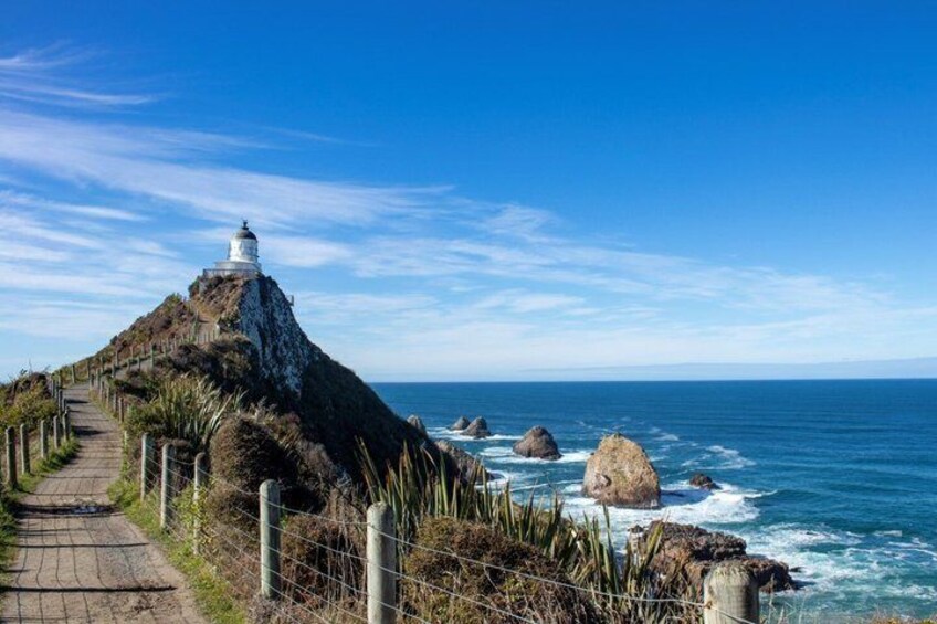 A coastal path leading to a lighthouse, surrounded by ocean waves and rocky outcrops. 5