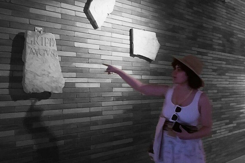 Una persona señalando una pared con una losa de piedra que tiene texto escrito. 4