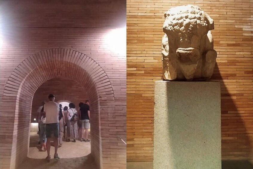 Un corredor de ladrillo abovedado con gente caminando. Una escultura de piedra se exhibe sobre un pedestal a la derecha. 2
