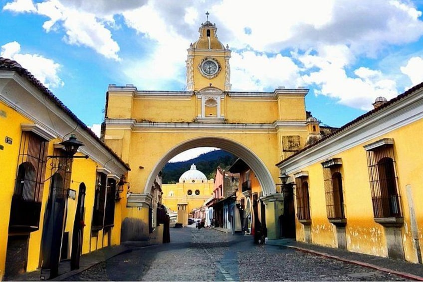 Una calle con un arco amarillo, una torre del reloj y edificios a ambos lados. 1