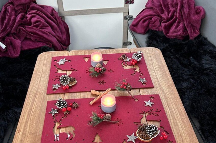Ett bord med röda bordsunderlägg i filt, dekorerade med tallkottar, bär och stjärnor, och två tända ljus. 2