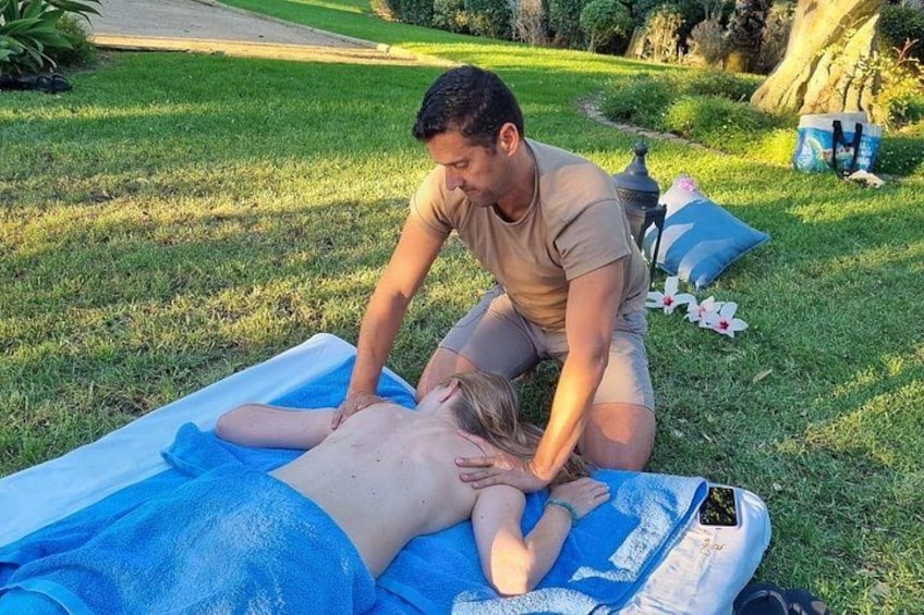 Iemand ontvangt een massage in de open lucht op een blauwe mat. 3