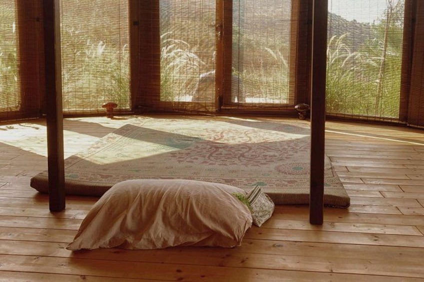 Een kamer met tatami matten, een lage houten tafel en een groot raam met uitzicht op groen. 2