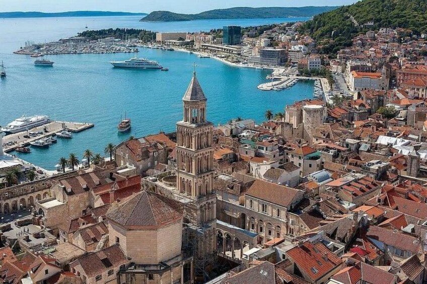 Una ciudad costera con una imponente torre de iglesia, un puerto deportivo con barcos y un paisaje montañoso al fondo. 4