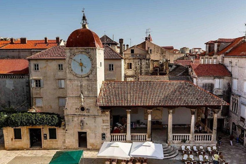 Un edificio histórico con una torre de reloj, un área de estar al aire libre cubierta y techos de tejas rojas. 3