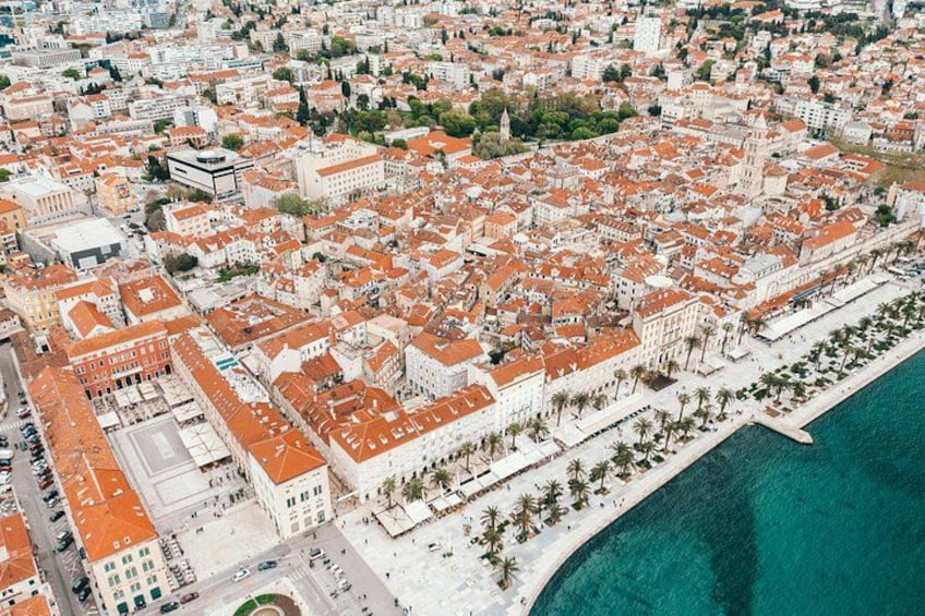 Vista aérea de una ciudad costera con arquitectura urbana densa, un paseo marítimo destacado y un mar azul cristalino. 5