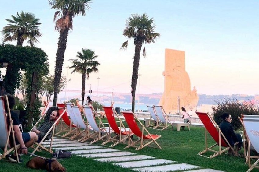 A beachside area with rows of red and white lounge chairs, palm trees, and a large statue in the background. 4