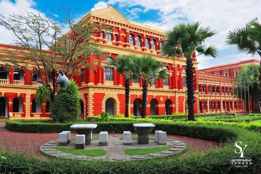 A red colonial-style building with a courtyard, palm trees, and a circular garden with stone benches. 2