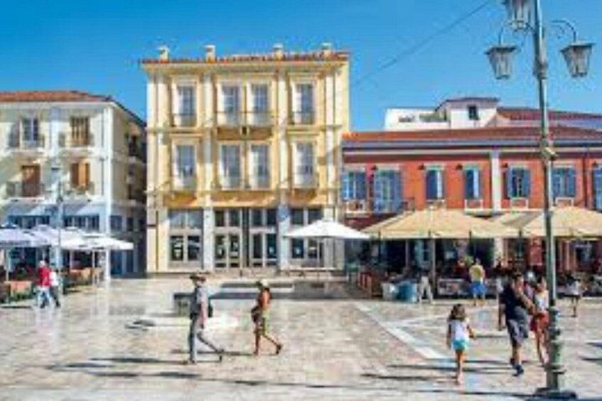 A plaza with buildings, outdoor seating, and people walking. 3