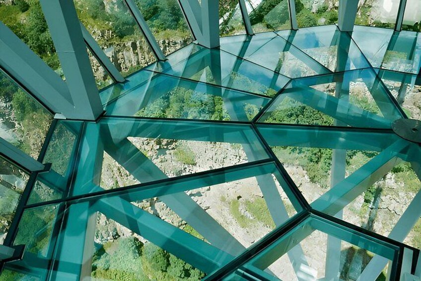 En glasstruktur med ett geometriskt mönster, omgiven av ett naturligt landskap. 3