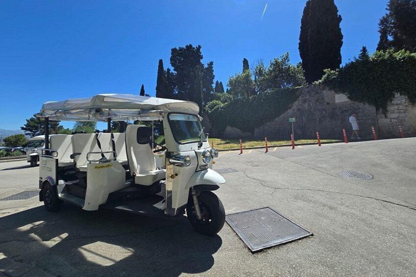 Un veicolo commerciale bianco parcheggiato su una superficie asfaltata, con una griglia metallica davanti, circondato da alberi e un cielo azzurro terso. 3