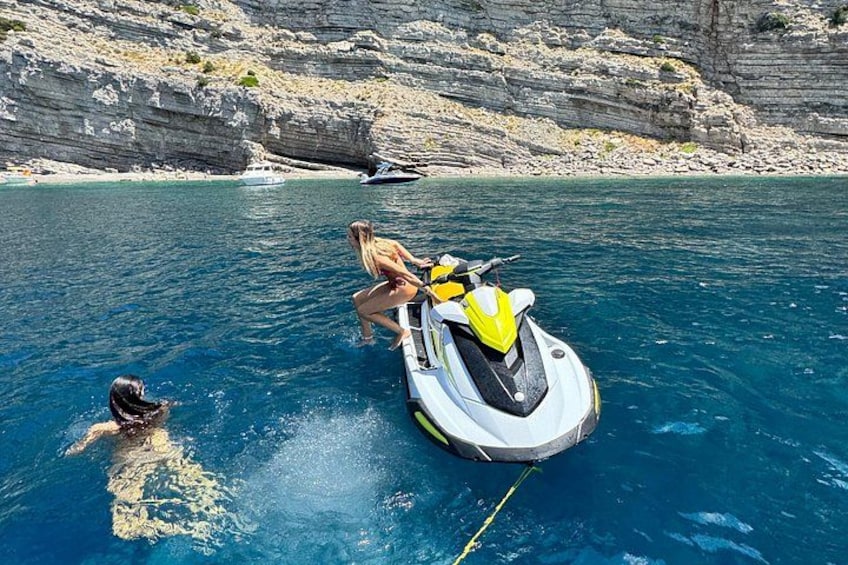 En person på en jetski i vandet med en klippefyldt kystlinje i baggrunden. 2