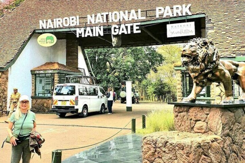 The Nairobi National Park main gate with a lion statue, a van, and a building labeled 'Paying Station'. 2