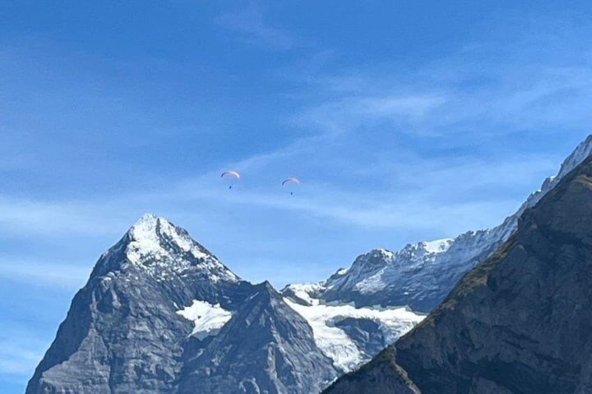 Ein Gebirge mit schneebedeckten Gipfeln und zwei Gleitschirmfliegern am Himmel. 5