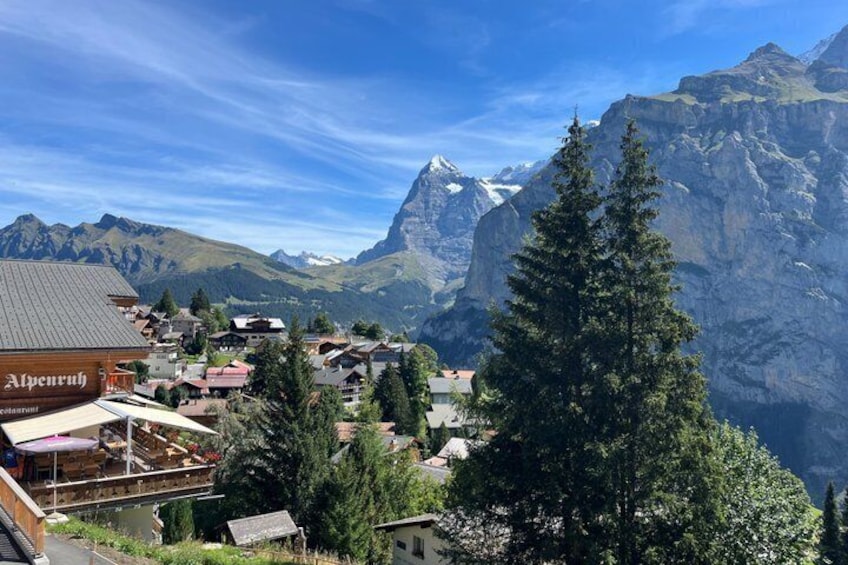 Ein Bergdorf mit Häusern, Bäumen und schneebedeckten Gipfeln im Hintergrund. 2