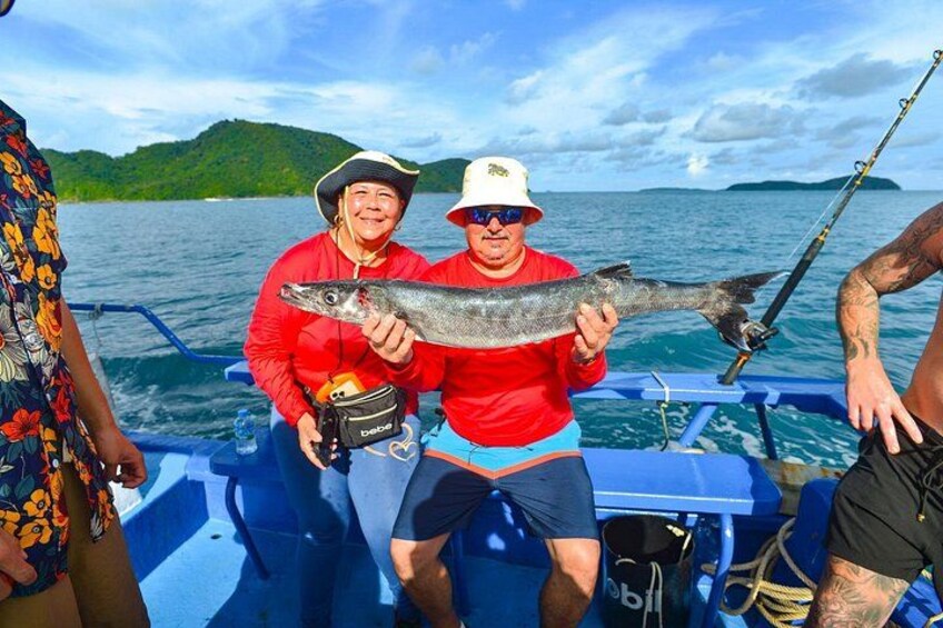 Two people on a boat holding a fish, with water and a distant island in the background. 3